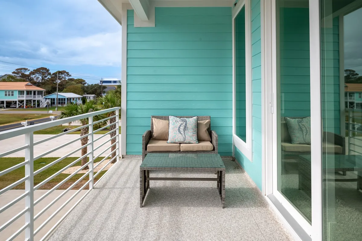 An inviting front porch scene shows turquoise walls, a charming outdoor seating area, and a coffee table, all bathed in gentle natural light. The relaxed setup suggests a perfect spot for morning coffee or evening breezes, connecting the interior hub to the outdoors.