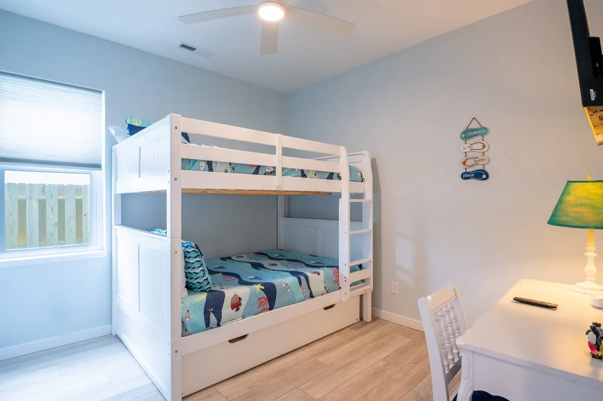 A lively bunkroom with full-over-full bunk beds, a trundle underneath, colorful bedding, desk and chair, and fun wall signs. The setup invites activities like sleepovers, studying, and play, making it a kids’ paradise.