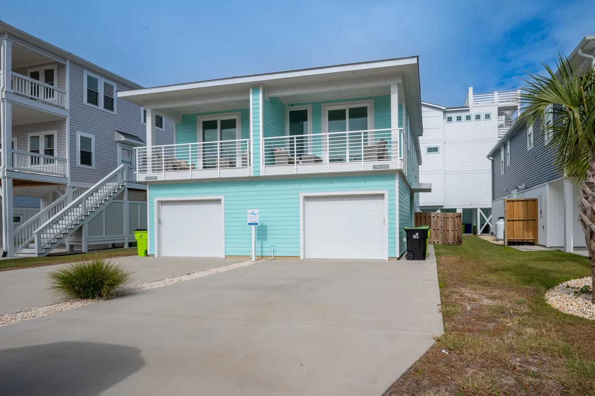 The image showcases a cheerful light blue beach house with inviting white railings, a spacious driveway, and swaying palm trees. The porch is perfect for relaxing while catching sunset views, and the home's exterior radiates a laid-back coastal vibe ideal for families.