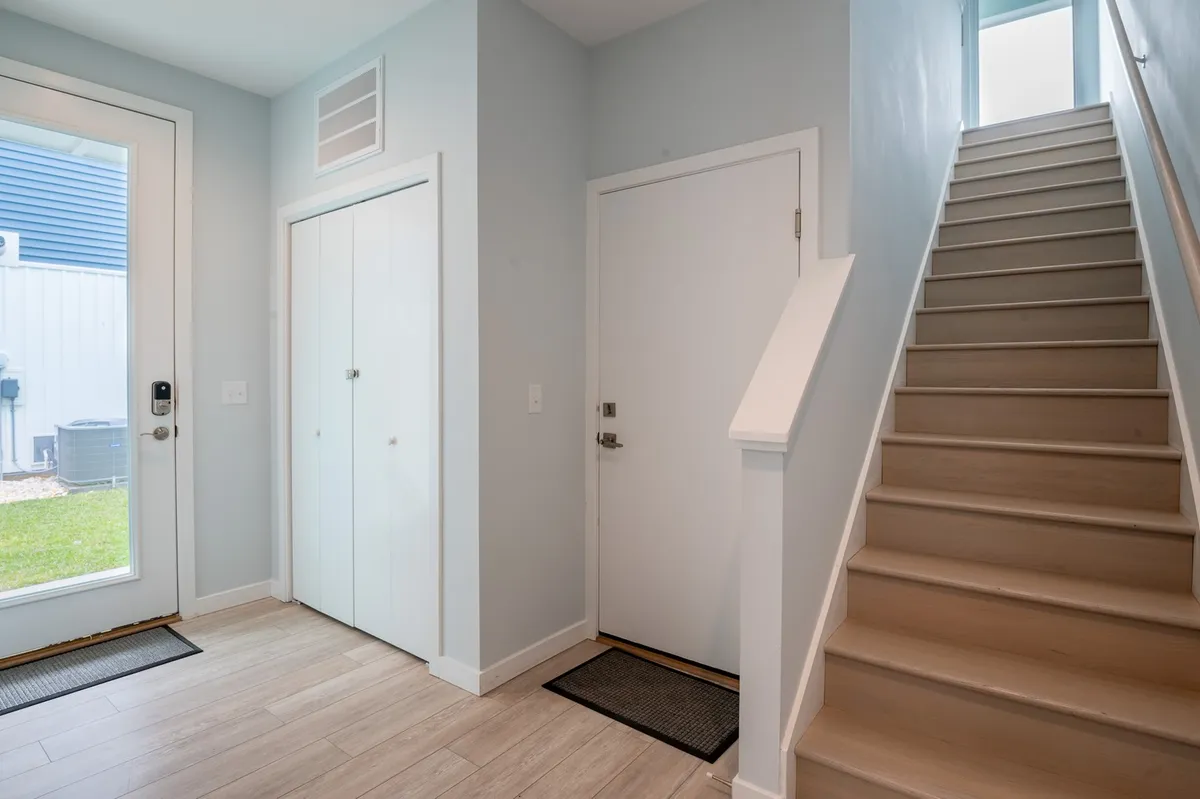 The image captures the home's front entryway, including a welcoming front door, visible stairs leading upward, and a closet door. The space is bright and inviting, giving a sense of a smooth and pleasant arrival environment.