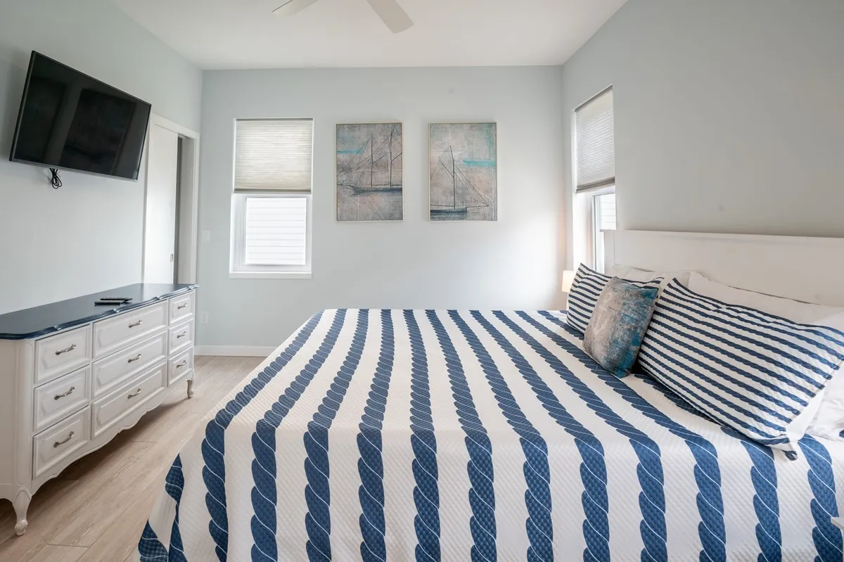 A tranquil bedroom with a king bed adorned with striped bedding, a Smart TV on the wall, and soft natural light streaming in. Artistic touches in the décor create a calm, inviting retreat after a day outdoors.