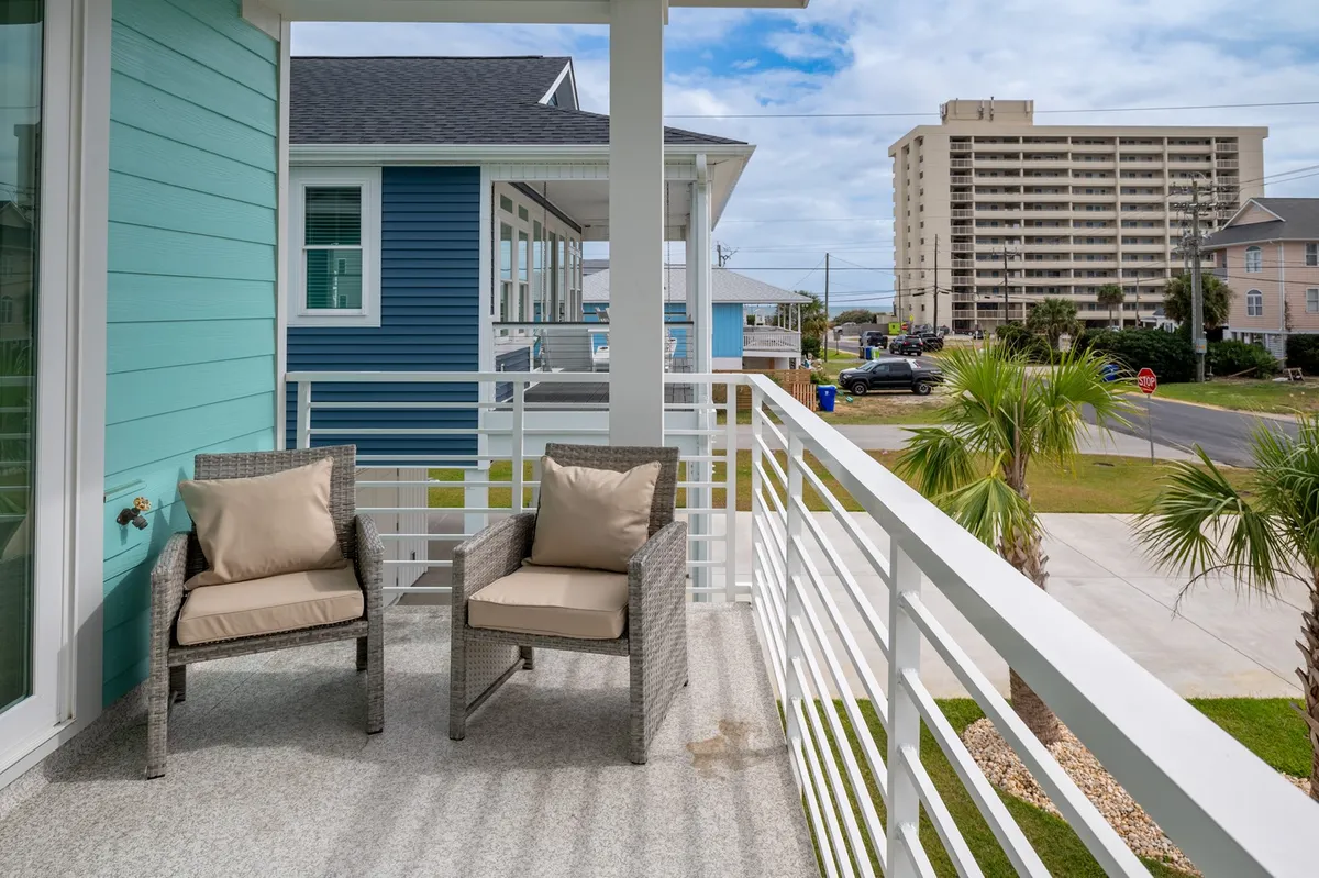 A cozy balcony with comfortable seating faces a blue exterior wall, surrounded by palm trees. It's designed for relaxation—perhaps a spot for parents to enjoy morning coffee or unwind after a day of adventure while soaking up the sea air.