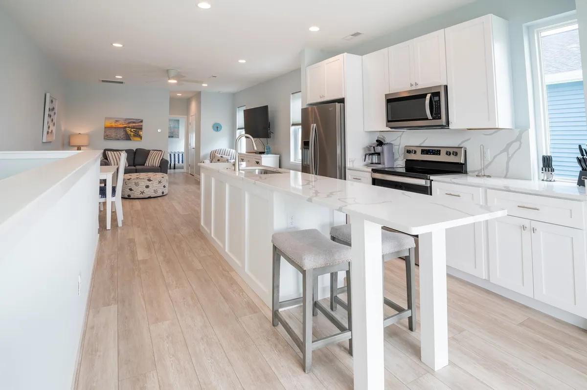 Centered on the gleaming kitchen island with bar seating and stainless steel appliances, this image captures the heart of the kitchen, where snacks and morning coffee can be enjoyed. The seating arrangement hints at casual breakfasts or socializing during meal prep.