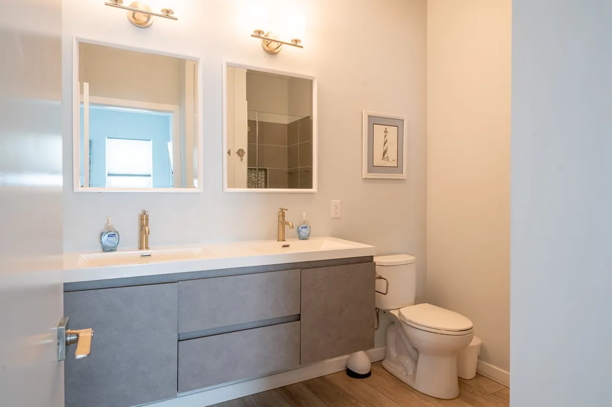 A modern bathroom featuring a double floating vanity with gold fixtures and large mirrors. The room feels serene and spa-like, ideal for shared routines or moments of private relaxation. The clean lines, soft lighting, and spacious layout emphasize comfort and luxury.