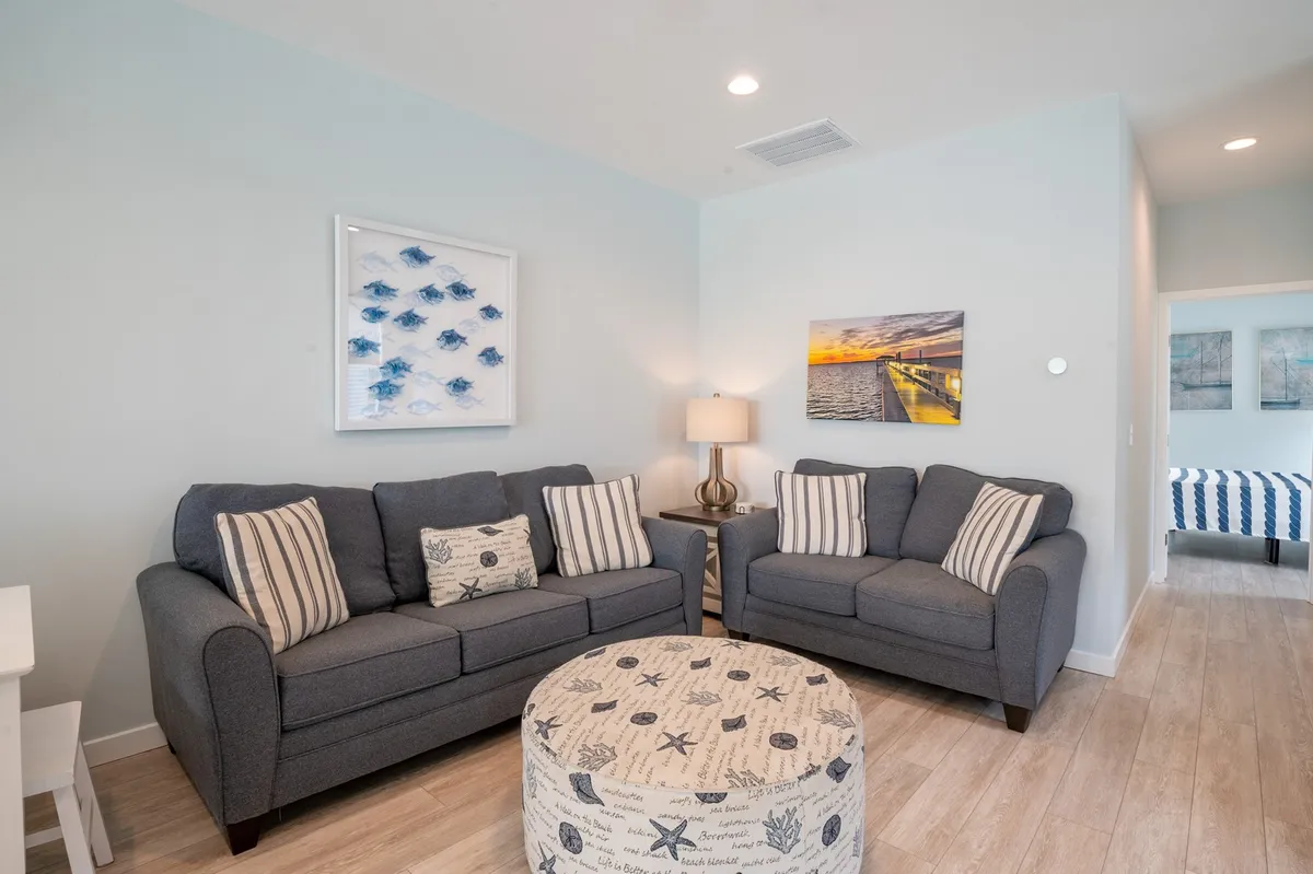 A cozy living area featuring two comfortable sofas, a round ottoman, tastefully selected wall art, and a soft lamp creates a space for relaxation and socializing. The inviting setting naturally encourages gathering with friends or unwinding after a day of adventure.