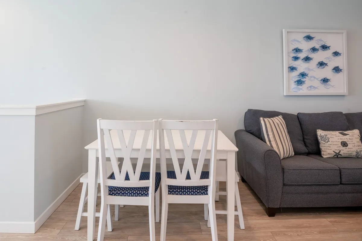 A welcoming dining area unfolds with a stylish table set for six, surrounded by comfortable chairs. In the background, the soft sofa and vibrant artwork connect this space to the larger living area, suggesting easy transitions from dining to relaxing.