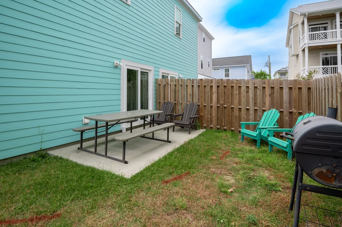 A fenced backyard featuring a picnic table, Adirondack chairs, grill, and wood fencing. The space is set up for outdoor dining, relaxation, and safe play—perfectly accommodating both people and their pets in a secure environment.