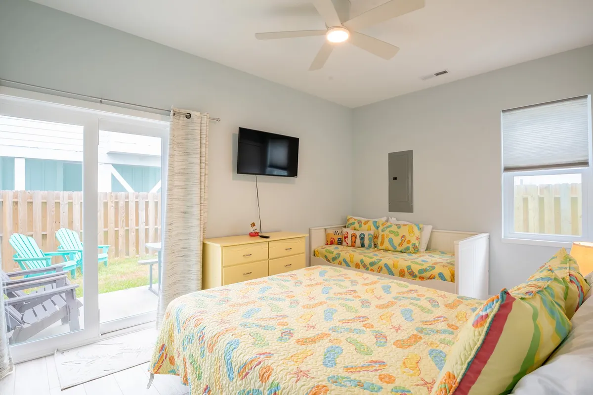 This image features a cheerful interior scene with a colorful bedspread, sofa bed, television, and a sliding glass door that opens to the outside. The door provides a visual connection between the cozy indoor setting and the potential for outdoor adventure.